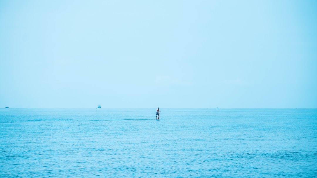 A person paddleboarding on a vast blue ocean, blurred horizon, emphasizing calm and serenity.