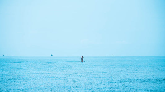 A person paddleboarding on a vast blue ocean, blurred horizon, emphasizing calm and serenity.